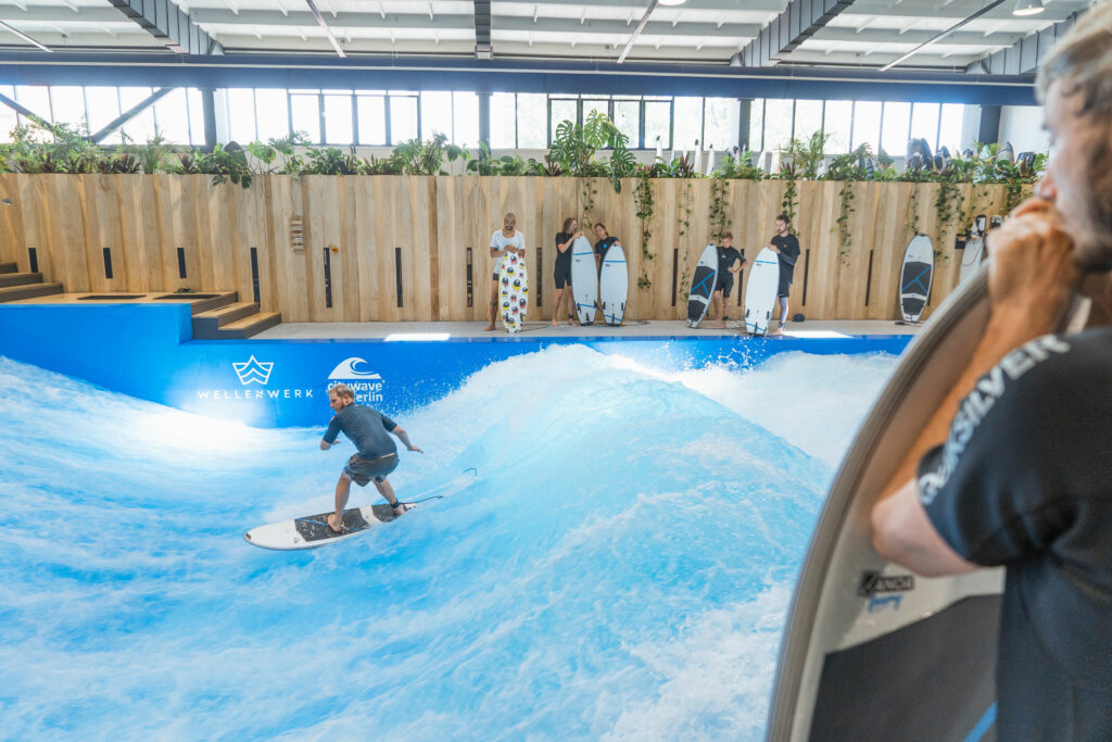 Surfer surft in Indoor Surfhalle auf der Welle