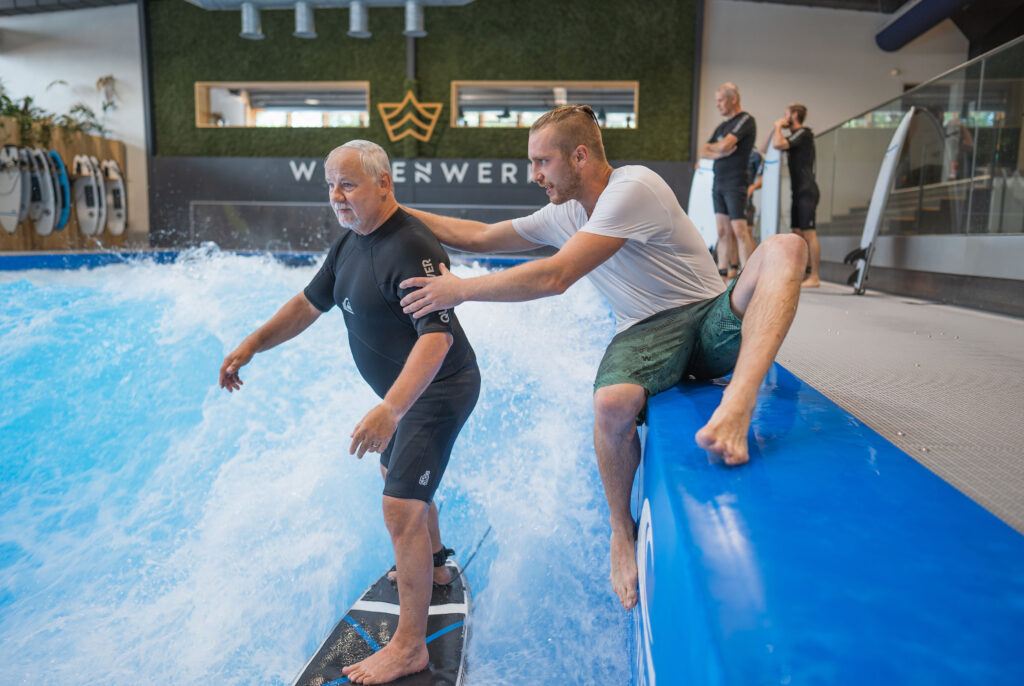 surf instructor helps surfer get on surfboard
