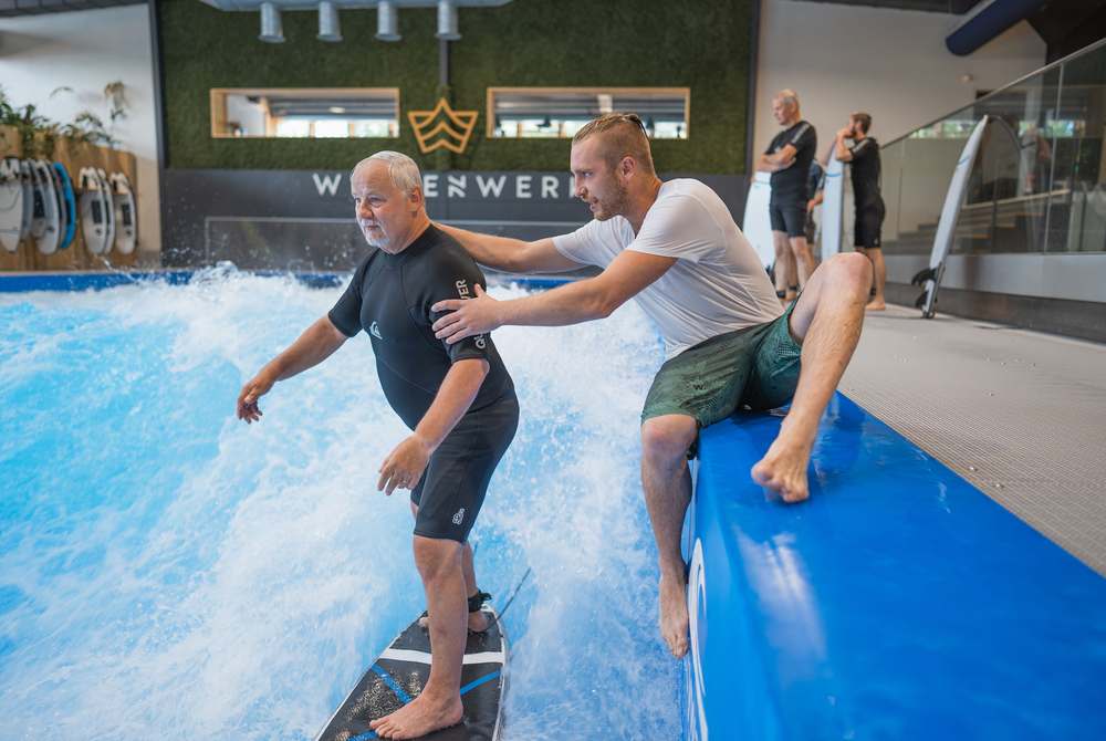 Anfänger bei seiner ersten Indoor-Surf-Session — der Coach stützt