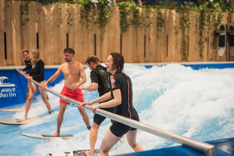 Beginner surfing with a support bar, coach assisting