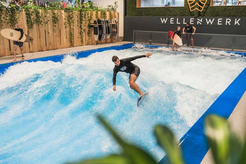 Surfer in voller Fahrt auf der Welle, Halle im Hintergrund